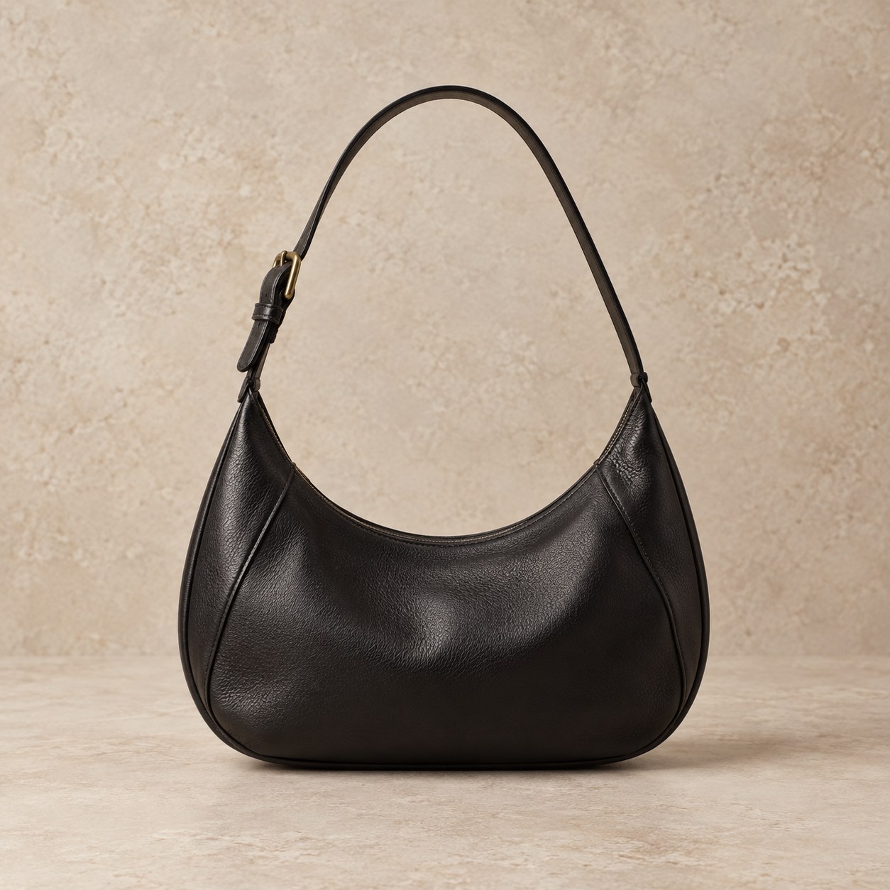 The Crescent, a curved black leather shoulder bag with a brass buckle